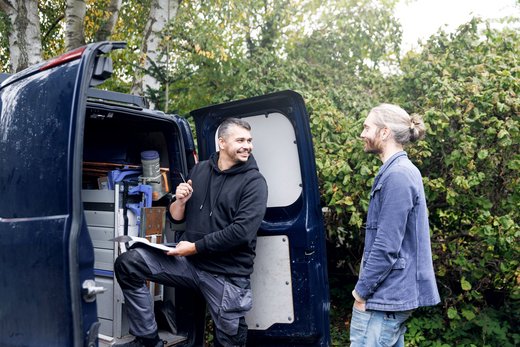 Zwei Männer unterhalten sich am Gepäckraum eines Lieferwagens. Innen Arbeitsgeräte.