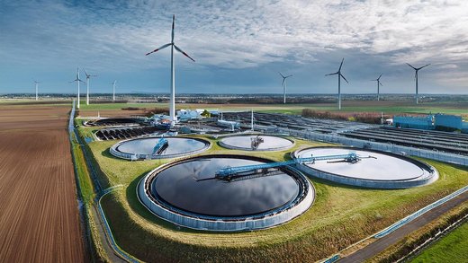 Ein Klärwerk mit Windkraftanlagen im Hintergrund.