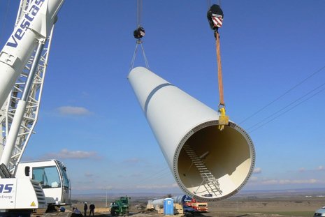 Der Mast einer Windkraftanlage wird von einem weißen Kran angehoben.