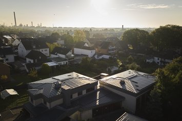 Kirchengebäude mit Photovoltaik-Solaranlagen auf den Dächern in einem Wohngebiet, im Hintergrund ist in weiter Entfernung ein Kraftwerk zu sehen.