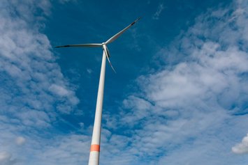 Windrad dreht sich vor blauem, leicht bewölktem Himmel.