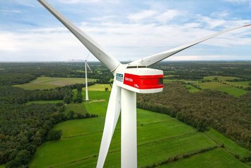 Nahe Drohnenaufnahme einer Windkraftanlage von hinten. An der linken Seite des Windradkopfes ist ein dunkelgrünes Logo mit der Aufschrift "Green Planet Energy" zu sehen.