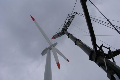Bodenansicht der Montage von Windturbinenflügeln an einer Windturbine mit Hilfe eines schwarzen Krans.