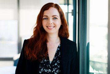 Eine Frau in einem weißen T-Shirt und einer schwarzen Jacke lächelt in die Kamera.